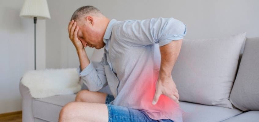 Мужчина сиди на диване и держится за поясницу