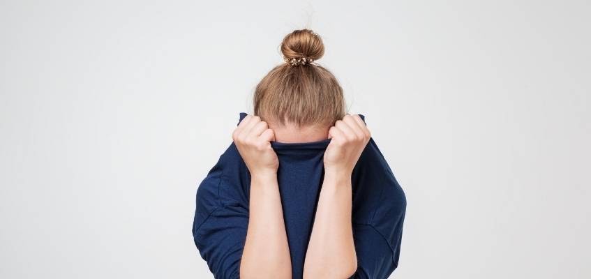 Девушка прячет лицо за кофтой