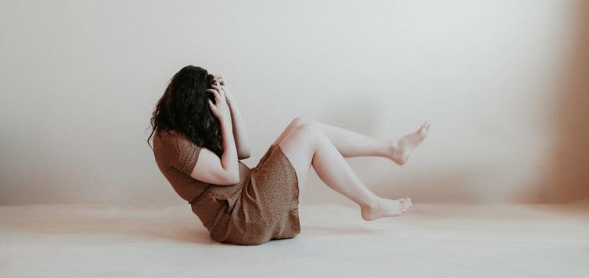 Девушка сидит на полу взявшись за лицо